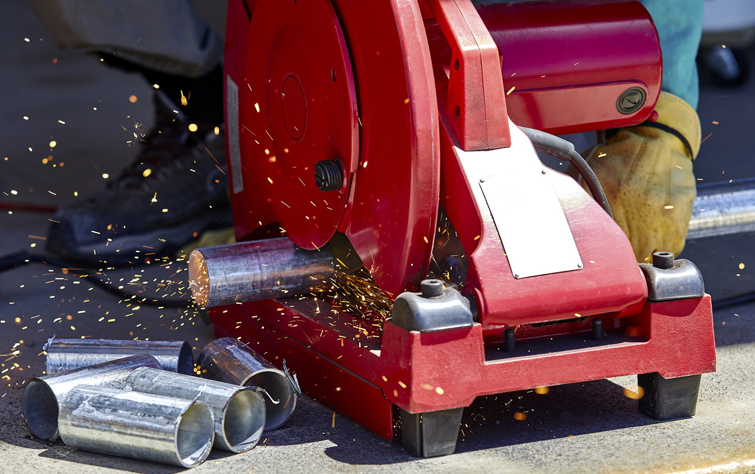 Photograph of someone cuttiing a metal pipe with a power saw.